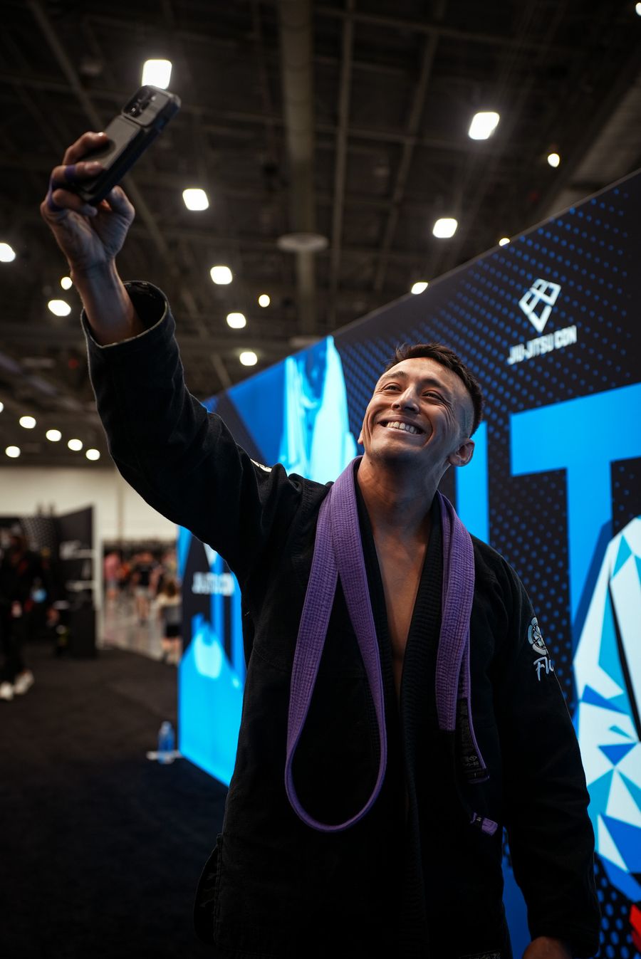 Atleta faixa-roxa sorrindo e tirando uma selfie em evento de Jiu-Jitsu